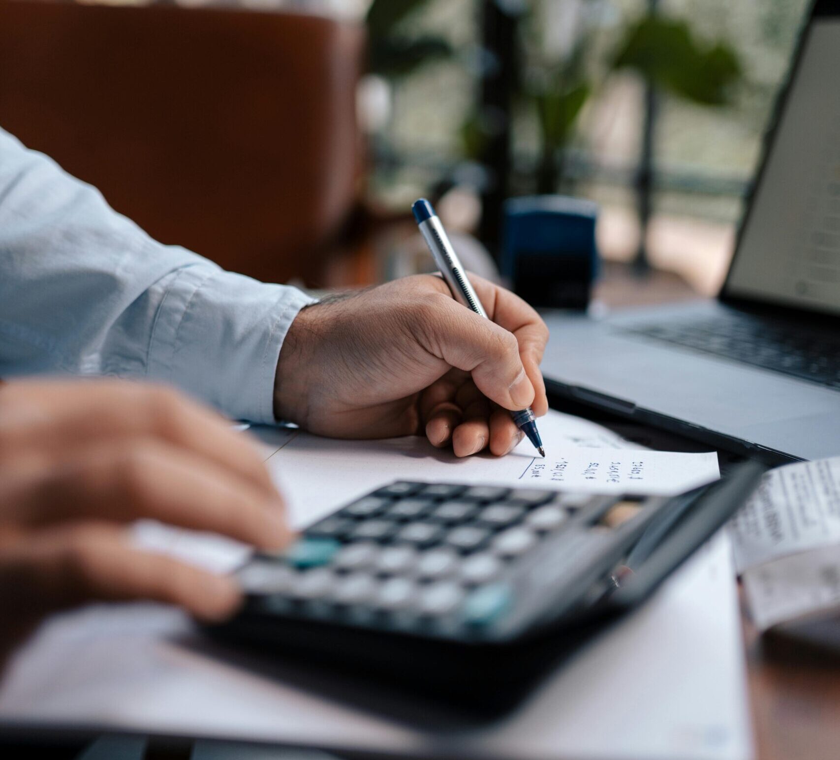 A person calculating finances with a calculator and pen on a desk indoors.