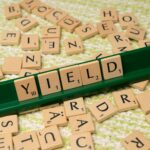 Scrabble tiles spelling 'Yield' on a rack among scattered letters.