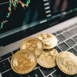 Close-up of gold Bitcoin coins on a laptop keyboard with a stock chart, symbolizing cryptocurrency market analysis.